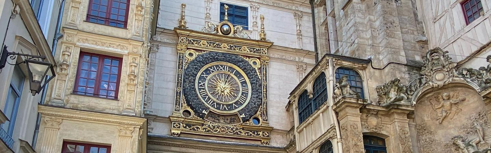 Zoomed in view of a building exterior with focus on an ornate clock. The clock is detailed with gold and is quite large.